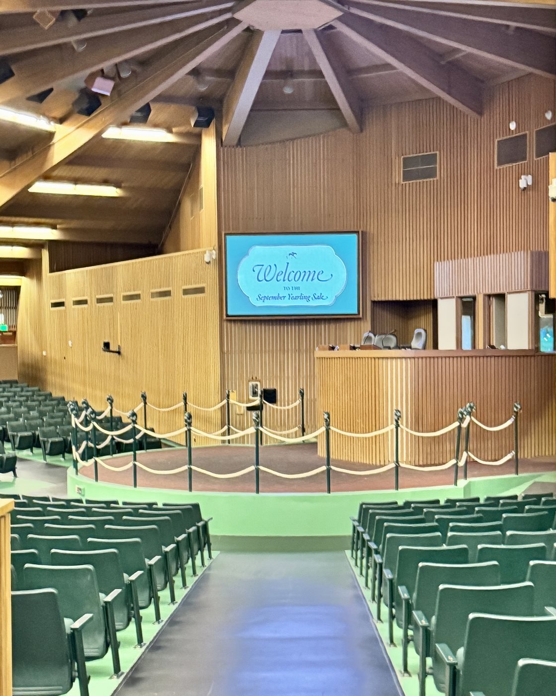The Keeneland sales pavilion before a session, with a sign reading Welcome to the September Yearling Sale above the auctioneer's stand and empty green seats around the ring.